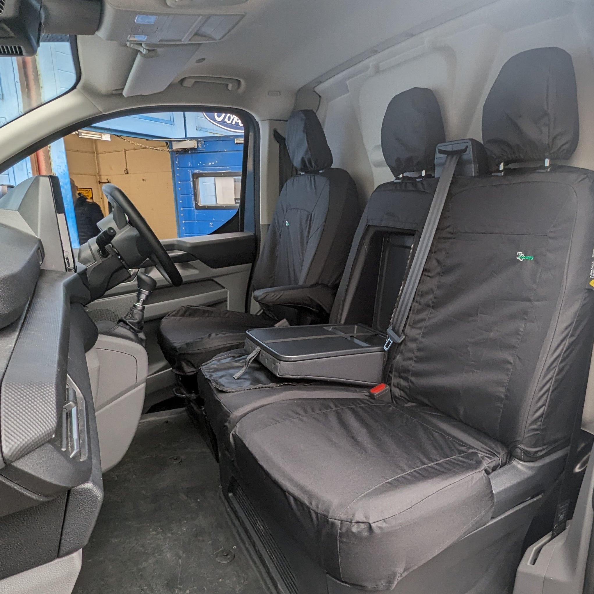 A black Ford Transit Custom seat cover fitted on a seat with an adjustable headrest.