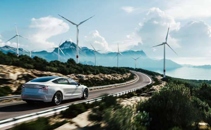 Electric car driving on road with wind turbines in mountainous background